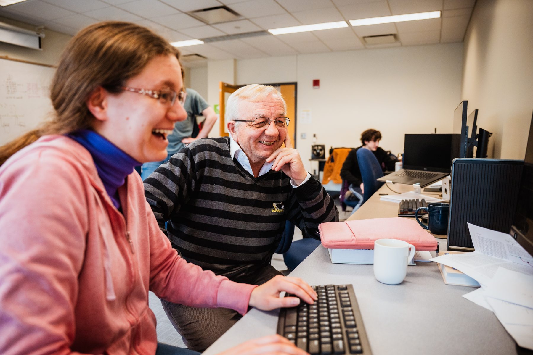 Prof. Soner Önder and a student laughing while looking at a monitor together.
