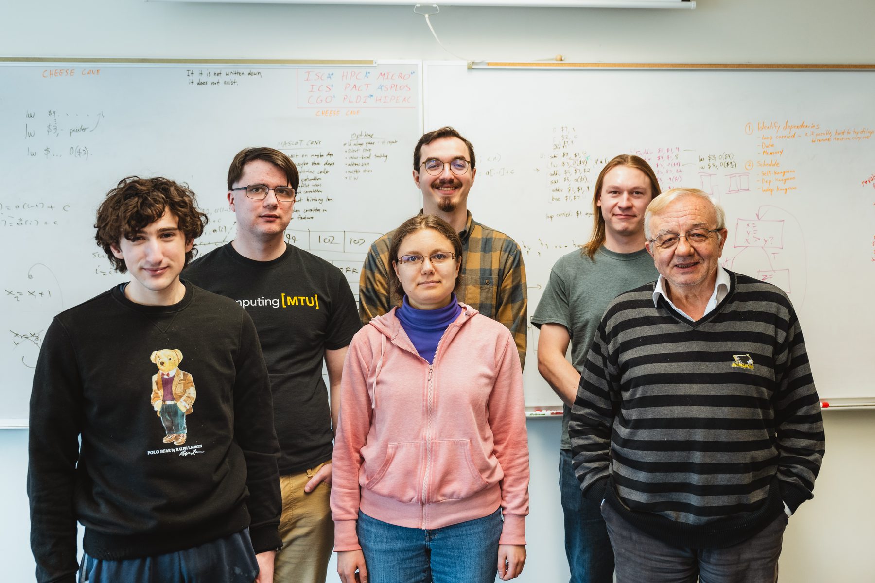 Five SCIA students and Prof. Soner Önder standing together in front of whiteboards covered in notes.