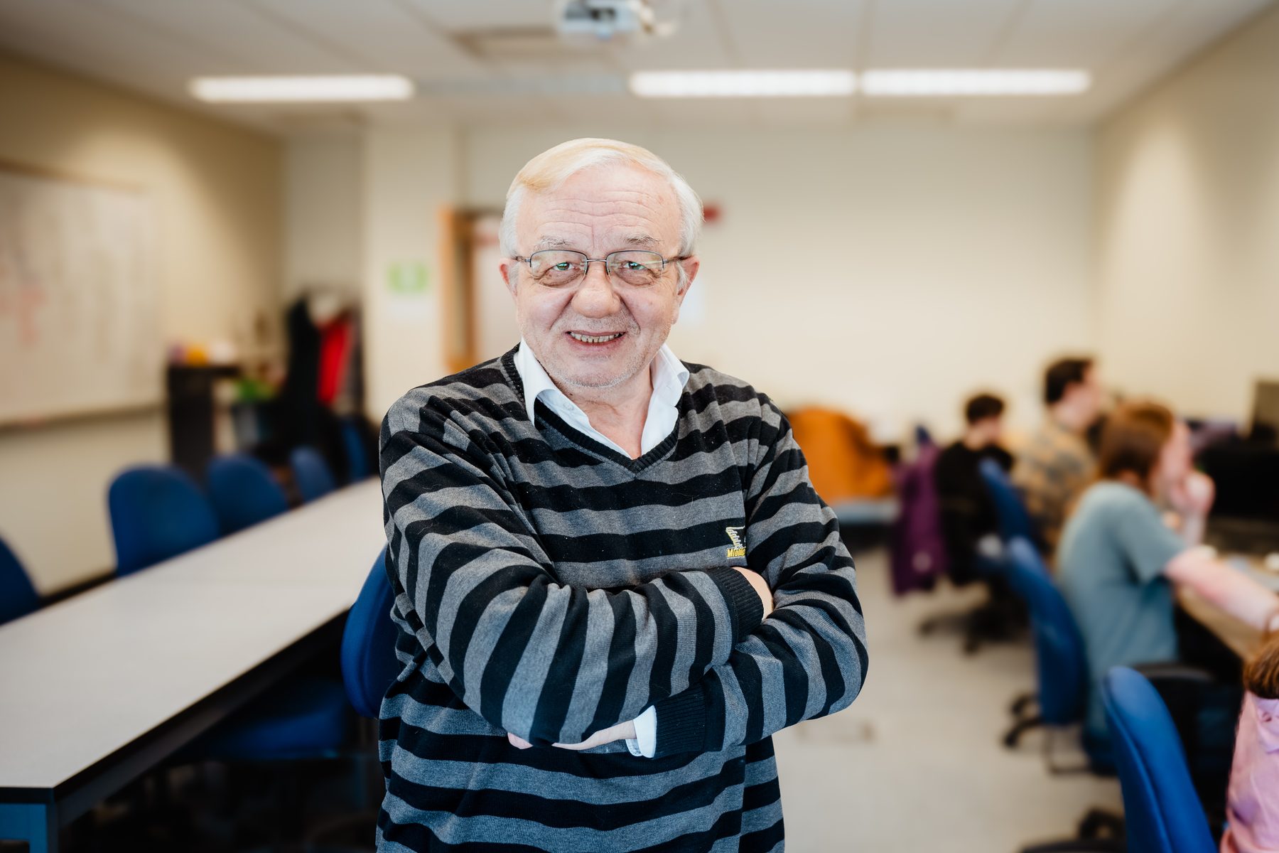 Prof. Soner Önder standing with arms crossed in the lab, students working in the background.